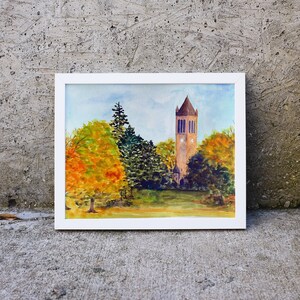 K&ouml;nnte beinhalten: Aquarellmalerei eines hohen Ziegelturms mit einem Zifferblatt, umgeben von Herbstlaub in Orange-, Gelb- und Gr&uuml;nt&ouml;nen. Der Turm steht vor einem blauen Himmel mit wei&szlig;en Wolken.