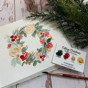 Puede incluir: Pintura de acuarela de una corona navide&ntilde;a con flores blancas y rojas, hojas verdes y bayas rojas. Se muestra una tarjeta con el texto "Cottage Christmas Watercolor Dot Samples" y muestras de color para verde pino, baya, crema y oro.