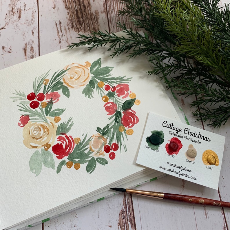 Puede incluir: Pintura de acuarela de una corona navide&ntilde;a con flores blancas y rojas, hojas verdes y bayas rojas. Se muestra una tarjeta con el texto "Cottage Christmas Watercolor Dot Samples" y muestras de color para verde pino, baya, crema y oro.