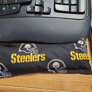 May include: Two black and yellow fabric wrist rests with the Pittsburgh Steelers logo and the word "Steelers" printed in yellow.