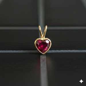 May include: A heart-shaped pendant with a vibrant red gemstone set in a gold-colored metal. The pendant has a simple, elegant design, with a polished finish. The gemstone is faceted, catching the light and creating a sparkling effect. The pendant is likely for a necklace.
