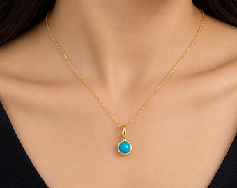 May include: A gold chain necklace featuring a small, round, bright turquoise pendant. The pendant is set in a polished gold bezel, suspended from a delicate gold link chain that rests against the collarbone area of the neck.