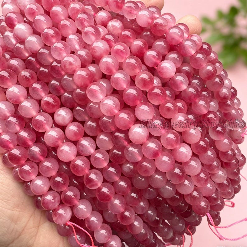 Puede incluir: Primer plano de una colecci&oacute;n de cuentas de piedras preciosas rosas. Las cuentas son redondas y tienen un aspecto transl&uacute;cido, con diferentes tonos de rosa. Las cuentas est&aacute;n ensartadas, lo que sugiere que son para hacer joyas.