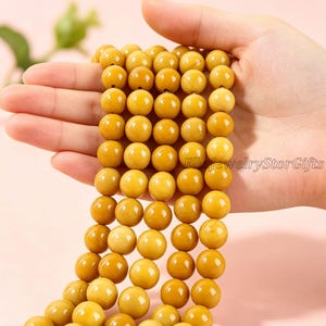 May include: A long strand of smooth, round, mustard yellow beads arranged in multiple vertical columns. The beads have a glossy finish and a uniform spherical shape, creating a consistent texture throughout the entire length of the beaded strand.