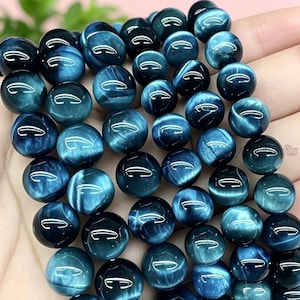 May include: A selection of polished, round beads in shades of deep blue and teal. The beads have a glossy finish and a unique, swirling pattern, suggesting a natural stone. These beads are ideal for jewellery making.