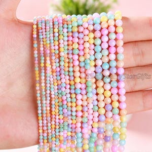 Puede incluir: Múltiples hileras de cuentas lisas y redondas en una variedad de colores pastel que incluyen rosa, amarillo, azul, verde y morado. Las cuentas están dispuestas en filas verticales de tamaños variados, creando un efecto degradado de esferas.