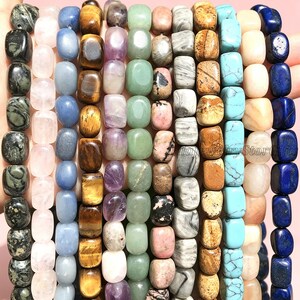 May include: Ten vertical strands of smooth, rectangular gemstone beads in various colours including dark green, pale pink, blue, brown tiger eye, purple, light green, mottled pink, grey, turquoise, and deep blue, arranged side by side.
