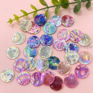 May include: A collection of circular abalone shell charms featuring iridescent, multi-colored surfaces with swirling patterns of blue, purple, pink, and green. Each flat, round piece includes a small pre-drilled hole for attachment.