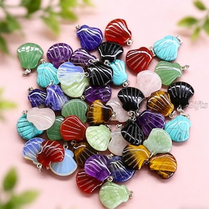 Peut inclure: Une collection de pendentifs en forme de coquillage en pierres précieuses de différentes couleurs, dont le rouge, le vert, le violet, le bleu et l'œil de tigre. Chaque pendentif a une boucle argentée pour l'attacher. Sur fond rose.