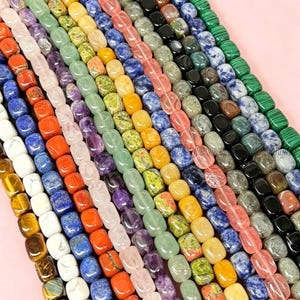 Puede incluir: Filas de cuentas de piedras preciosas de colores en varios tonos, incluyendo azul, naranja, amarillo, verde y morado. Las cuentas rectangulares están ensartadas, creando una vibrante exhibición de componentes de joyería de piedra natural.
