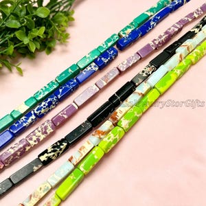 Pode incluir: Fios de contas retangulares em várias cores, incluindo verde, azul, roxo, preto e verde limão. As contas têm um padrão salpicado ou marmorizado. O texto "iaJewelryStorGifts" é visível. Ideal para fazer joias.