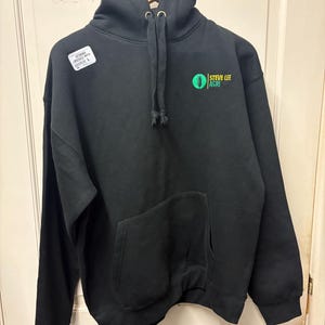 May include: Black hoodie with a front pocket and drawstring hood. The hoodie features the text "STEVE LEE AGRI" in green and white on the front. A white tag with the size "L" is attached to the hoodie.