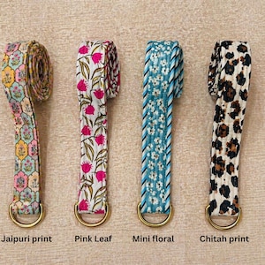 May include: Four fabric straps with gold-tone D-rings. The first features a multi-coloured Jaipuri print, the second a white background with pink leaf patterns, the third a blue floral print with striped edges, and the fourth a black and tan cheetah print.