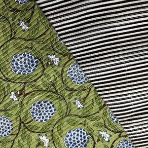 Puede incluir: Una tela textil que presenta dos patrones distintos. Una sección muestra un fondo verde con un estampado repetitivo de racimos florales azules y enredaderas marrones. La sección adyacente presenta un patrón de rayas finas paralelas en blanco y negro.