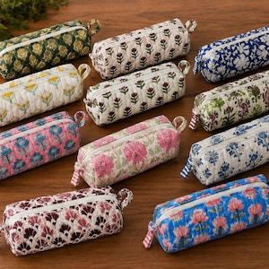 Könnte beinhalten: Eine Sammlung von zehn zylindrischen, gesteppten Stiftemäppchen mit verschiedenen floralen und geometrischen Blockdruckmustern in Farben wie Grün, Rosa, Blau und Creme. Jedes Mäppchen hat einen Reißverschluss und eine kleine Stoffschlaufe am Ende.