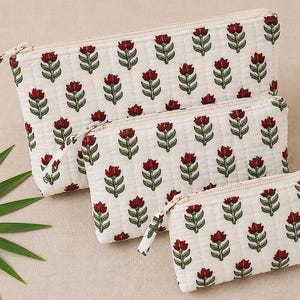 May include: A set of three rectangular zippered pouches in varying sizes, featuring a quilted off-white fabric with a repeating pattern of small red flowers and green stems. Each pouch has a matching off-white zipper closure and fabric pull.