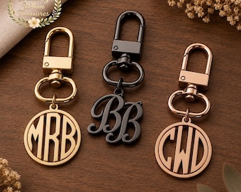 May include: Three metal keychains with lobster claw clasps. The left keychain is gold with a circular monogram reading MRB. The center keychain is black with a script monogram reading BB. The right keychain is rose gold with a circular monogram reading CWD.