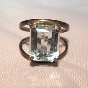 May include: A silver ring with a large, clear, rectangular aquamarine gemstone.
