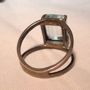 May include: A silver ring with a light blue rectangular gemstone set in a bezel setting.