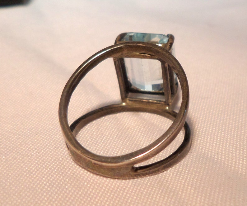 May include: A silver ring with a light blue rectangular gemstone set in a bezel setting.