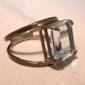 May include: A silver ring with a large, clear, rectangular aquamarine gemstone set in a cage-like design.