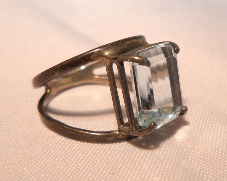 May include: A silver ring with a large, clear, rectangular aquamarine gemstone set in a cage-like design.