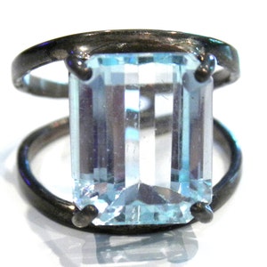 May include: A silver ring with a large, clear, light blue aquamarine gemstone set in a bezel setting. The ring has a simple, modern design.