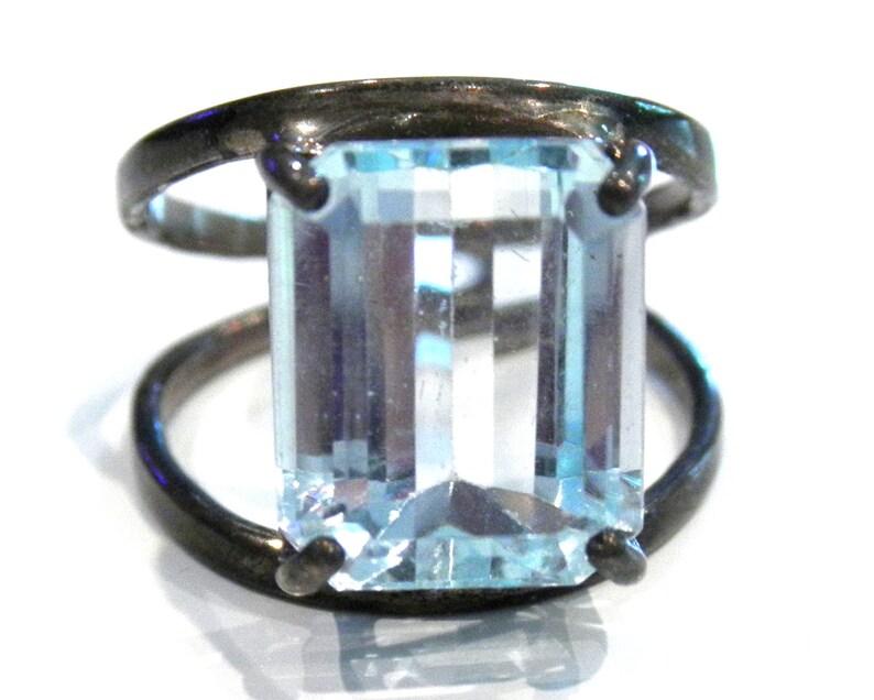 May include: A silver ring with a large, clear, light blue aquamarine gemstone set in a bezel setting. The ring has a simple, modern design.