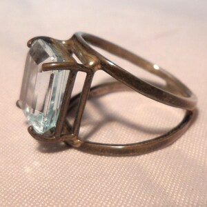 May include: A silver ring with a large, clear, rectangular aquamarine gemstone set in a cage-like design.