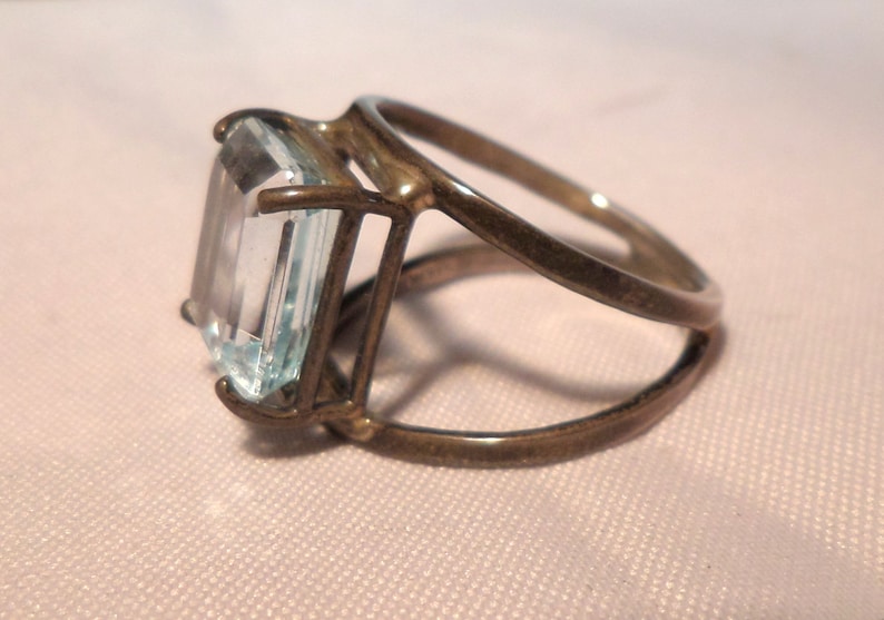 May include: A silver ring with a large, clear, rectangular aquamarine gemstone set in a cage-like design.