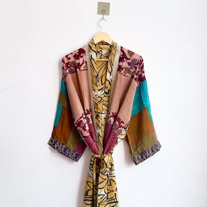 Peut inclure: Un peignoir kimono à manches longues présentant un motif patchwork avec divers panneaux de tissu dans des tons jaune moutarde, bordeaux, bleu sarcelle et marron. Le vêtement comprend une ceinture assortie et un mélange de motifs floraux.