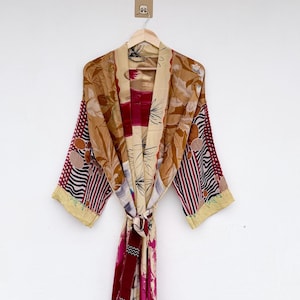 May include: A long-sleeved kimono robe featuring a patchwork design with various patterns and colors including tan, deep red, black, and white. The garment has a wide collar, a tie-waist belt, and a mix of floral, striped, and geometric prints.