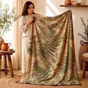 May include: A rectangular throw blanket featuring a detailed botanical print of green fern leaves and various foliage patterns set against a light beige background. The fabric displays a repeating nature-inspired design with multiple leaf shapes.