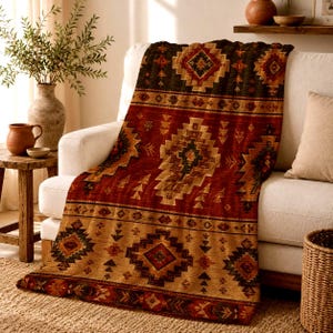 May include: A rectangular throw blanket featuring a repeating geometric pattern in shades of deep red, dark brown, and tan. The design includes diamond shapes, triangles, and horizontal bands, creating a textured appearance across the fabric.