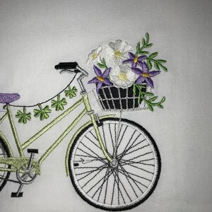 May include: A green bicycle with a basket full of white and purple flowers. The bicycle has a green frame and white wheels.