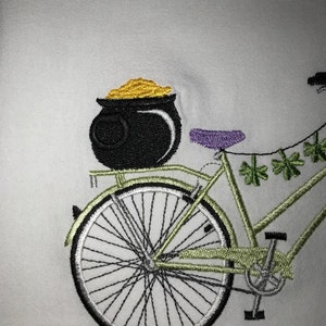 May include: A green bicycle with a pot of gold on the back rack. The bicycle has a purple seat and a string of shamrocks hanging from the handlebars.