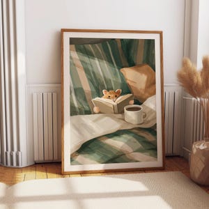 Pu&ograve; includere: Una stampa artistica incorniciata raffigura un criceto che legge a letto. L'illustrazione presenta un criceto marrone che tiene in mano un libro, una tazza di caff&egrave; e lenzuola a righe verdi e beige. L'opera &egrave; incorniciata in una cornice di legno.