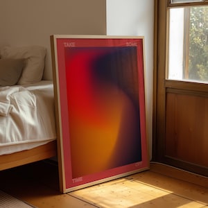 May include: A framed art print with an abstract design in shades of red, orange, and purple. The words "TAKE SOME TIME OFF" are printed in white along the frame. The print is leaning against a wall near a bed. The frame is a light wood color.