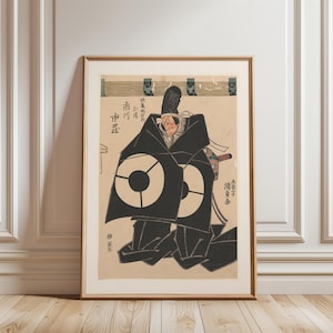 May include: Framed Japanese woodblock print featuring a Kabuki actor in a black robe with large white circular designs. The print has a beige background with Japanese text and is set in a gold frame.