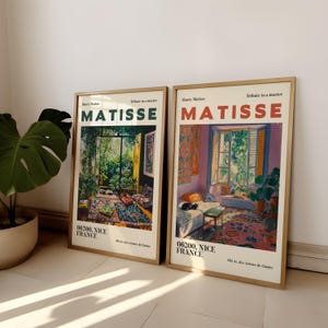 Könnte beinhalten: Zwei gerahmte Kunstdrucke mit farbenfrohen Innenszenen im Stil von Matisse. Das Wort "MATISSE" ist fett gedruckt. Die Drucke befinden sich in goldenen Rahmen und lehnen an einer weißen Wand. Eine Hommage an den Meister.