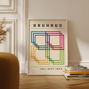 May include: A framed Bauhaus art print featuring overlapping colorful squares in blue, red, green, yellow, and purple. The print has the word "BAUHAUS" at the top and "JULI-SEPT 1923" at the bottom. The print is displayed on a wooden floor.
