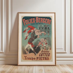 Puede incluir: Póster vintage enmarcado que anuncia Folies Bergere, con ilustraciones de acróbatas y luchadores. El póster tiene un fondo turquesa con texto rojo y beige. El póster está en un marco dorado y se apoya contra una pared blanca y un suelo de madera.