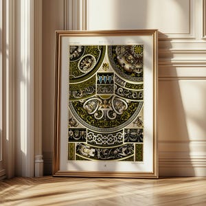 May include: A framed vintage print with detailed black, gold, and green ornamental designs. The print showcases intricate patterns, including floral and geometric shapes, within a gold frame. The artwork is displayed against a white wall and wooden floor.