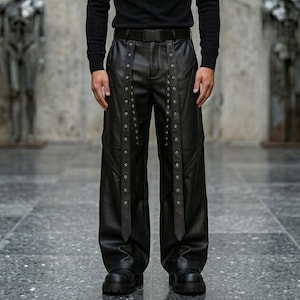 High-quality black leather trousers for men, featuring a baggy fit, gothic hardware details, and long hanging straps with metal silver eyelets.
