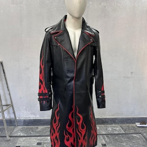 Pu&ograve; includere: Cappotto lungo in pelle nera con design a fiamme rosse. Il cappotto presenta un colletto a revers, finiture rosse e chiusure con bottoni. Le fiamme rosse sono dipinte sulle maniche e sul davanti. Il cappotto &egrave; esposto su un manichino.