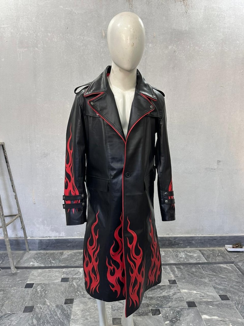 Pu&ograve; includere: Cappotto lungo in pelle nera con design a fiamme rosse. Il cappotto presenta un colletto a revers, finiture rosse e chiusure con bottoni. Le fiamme rosse sono dipinte sulle maniche e sul davanti. Il cappotto &egrave; esposto su un manichino.