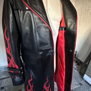 Pu&ograve; includere: Cappotto lungo in pelle nera con disegni di fiamme rosse sulle maniche e sul davanti. Il cappotto ha una fodera e finiture rosse, con dettagli di bottoni argentati. Un cappotto elegante.