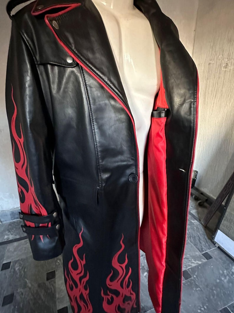 Pu&ograve; includere: Cappotto lungo in pelle nera con disegni di fiamme rosse sulle maniche e sul davanti. Il cappotto ha una fodera e finiture rosse, con dettagli di bottoni argentati. Un cappotto elegante.