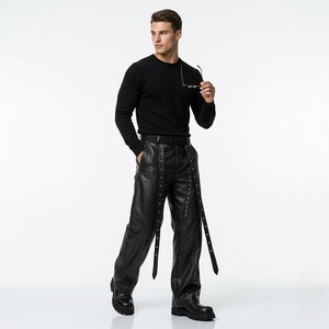 Fashionable men's black leather punk pants with a wide-leg cut and multiple metal eyelet straps, shown in a professional modeling pose on a clean white background.