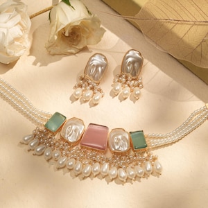 Könnte beinhalten: Elegantes Schmuckset mit einer Perlenkette und passenden Ohrringen. Die Kette hat ein mehrsträngiges Design mit quadratischen rosa, grünen und weißen Steinen. Die Ohrringe und die Kette haben baumelnde Perlenakzente.